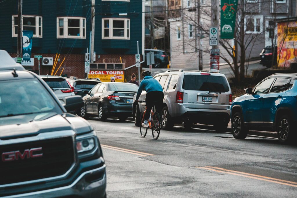 A man cycling on a busy urban street filled with vehicles during the day.