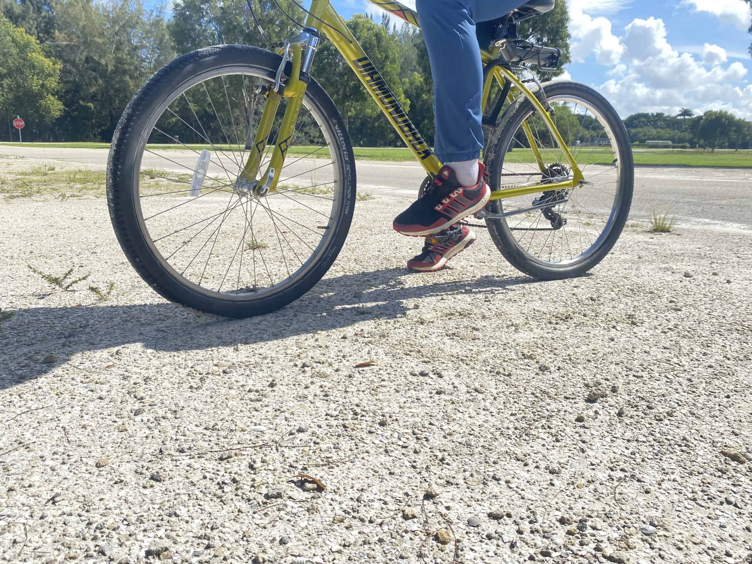 Bright yellow mountain bike on a gravel path with a rider wearing black and red athletic shoes and blue jeans.