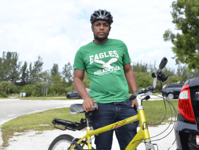 Mountain biking enthusiast wearing a green Eagles Philadelphia t-shirt, standing with a yellow bicycle outdoors.