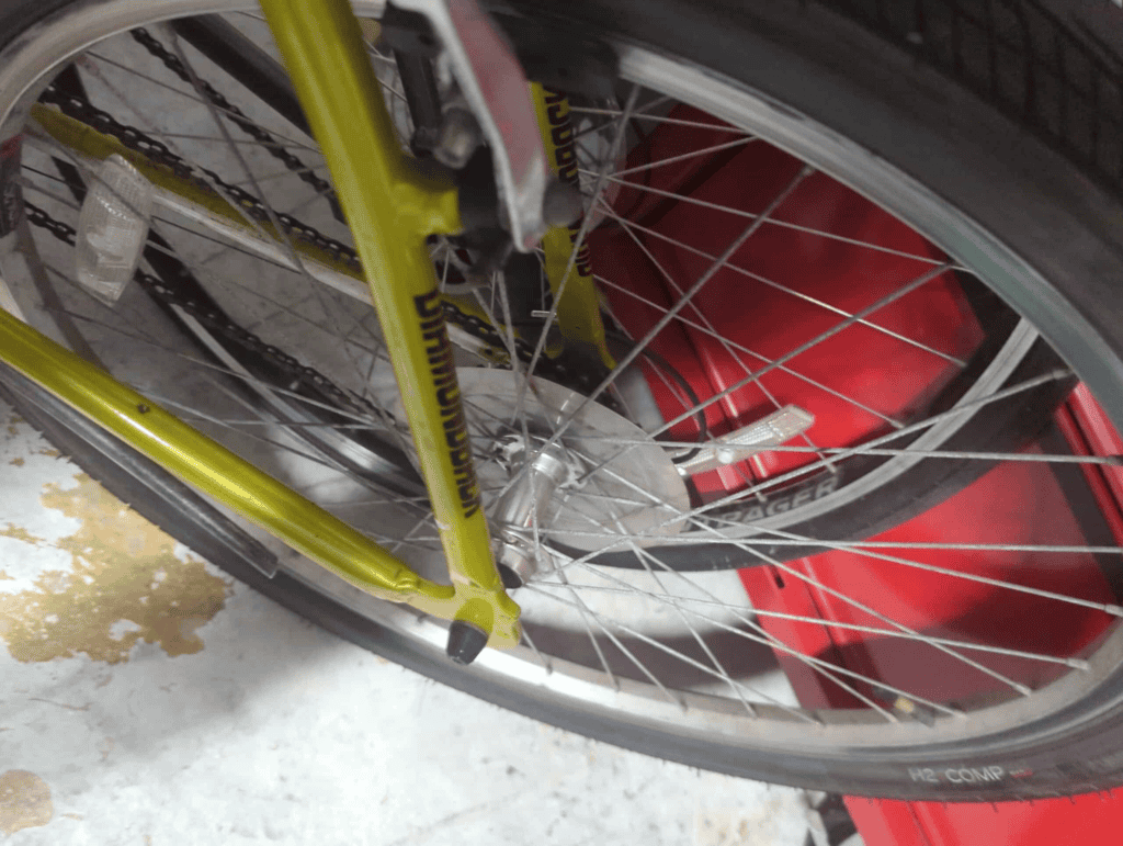 Yellow bicycle wheel with front fork and spokes, parked next to a red vehicle.