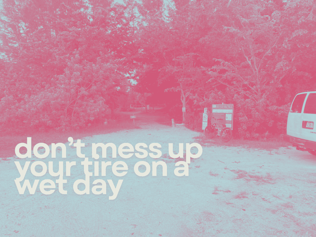 Muddy trail entrance at a scenic outdoor park with trees and informational signs.