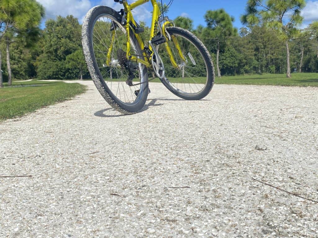 Bright yellow mountain bike on gravel trail in park with green trees and blue sky.