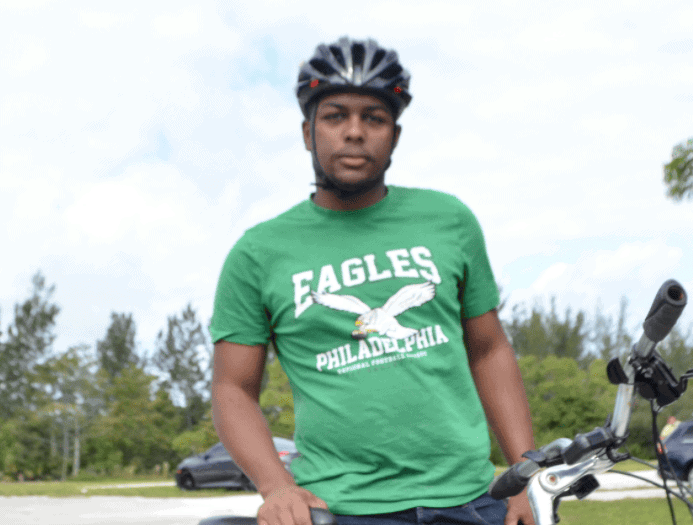 Mountain biking enthusiast wearing a green Eagles Philadelphia t-shirt, standing with a yellow bicycle outdoors.